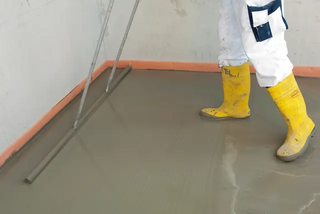 Das Bild zeigt einen Verarbeiter, der eine Schicht Zementschnellestrich glatt auf dem Boden verstreicht.